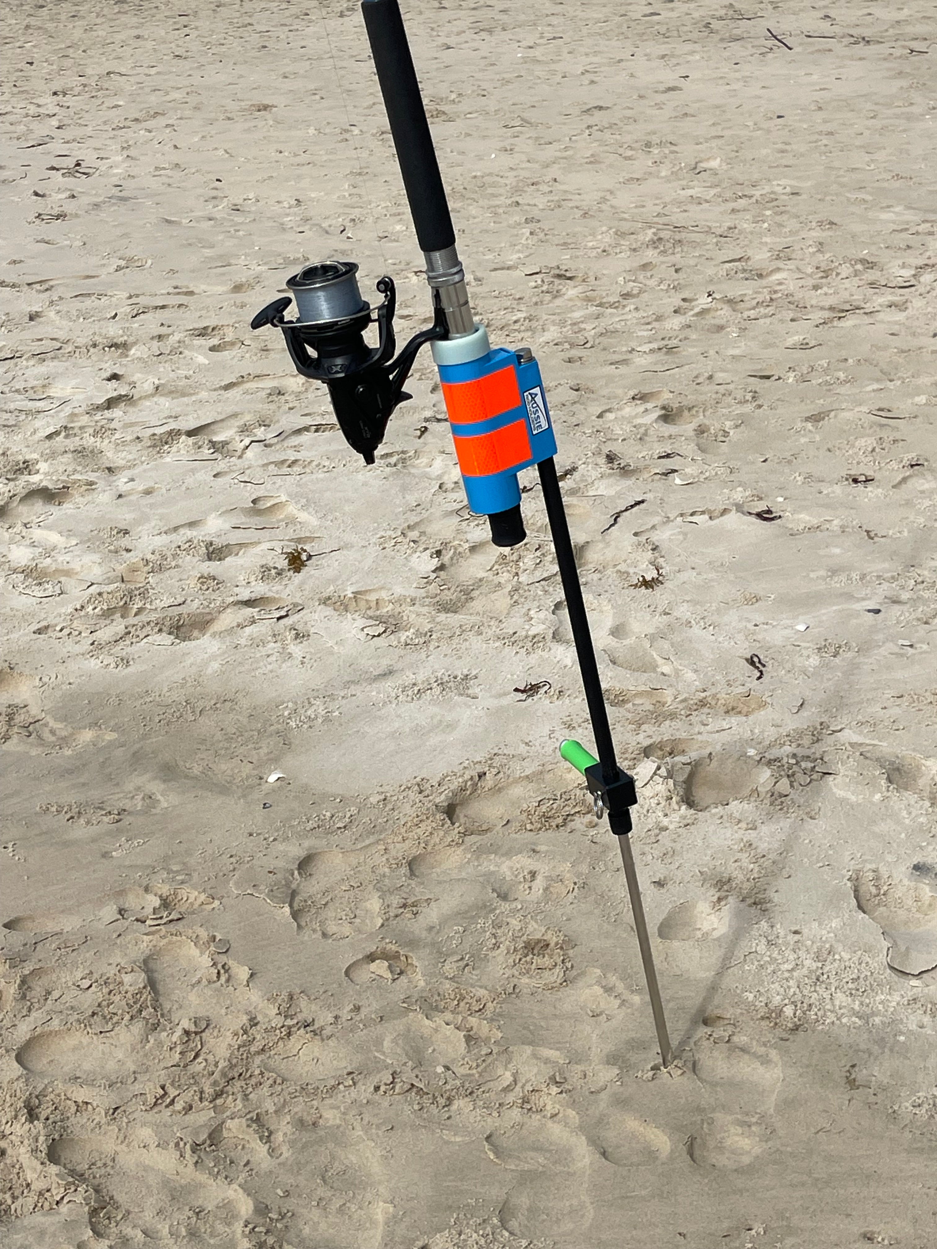Fishing rod holder with glow in the dark reel guard on sandy beach