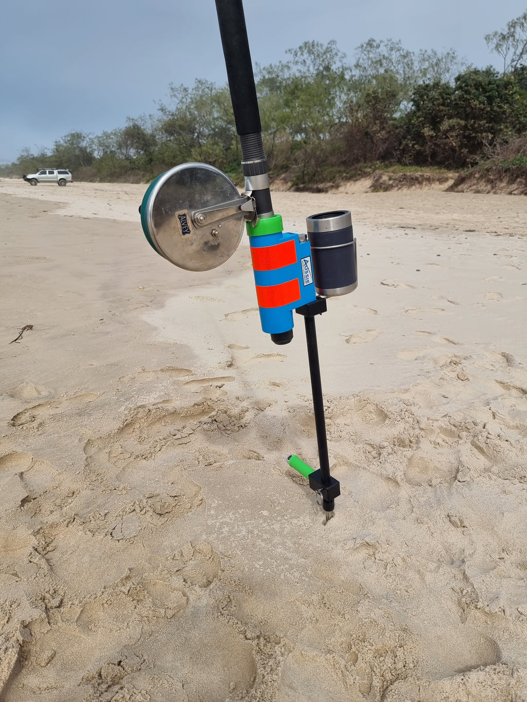 Fishing rod and reel in fibreglass fishing rod holder with beer holder on beach with 4wd in background