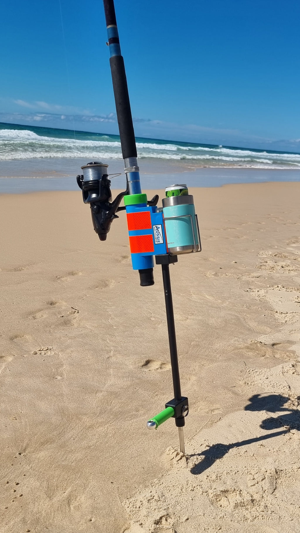 Fishing rod with reel and sand spike on a sandy beach with ocean waves in the background