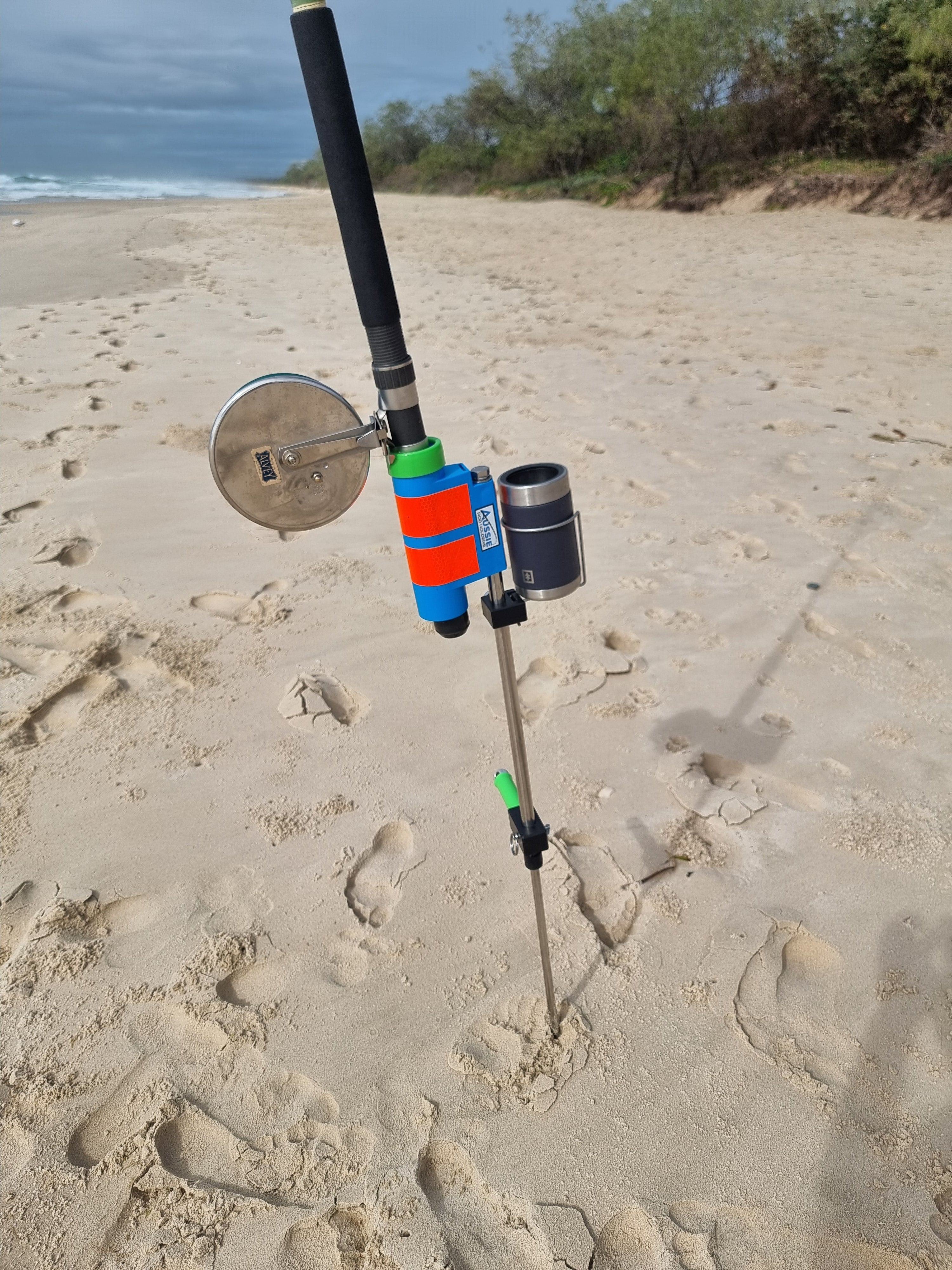 Fishing rod with colorful reel in Aussie Rod Holder with drinks holder on sandy beach