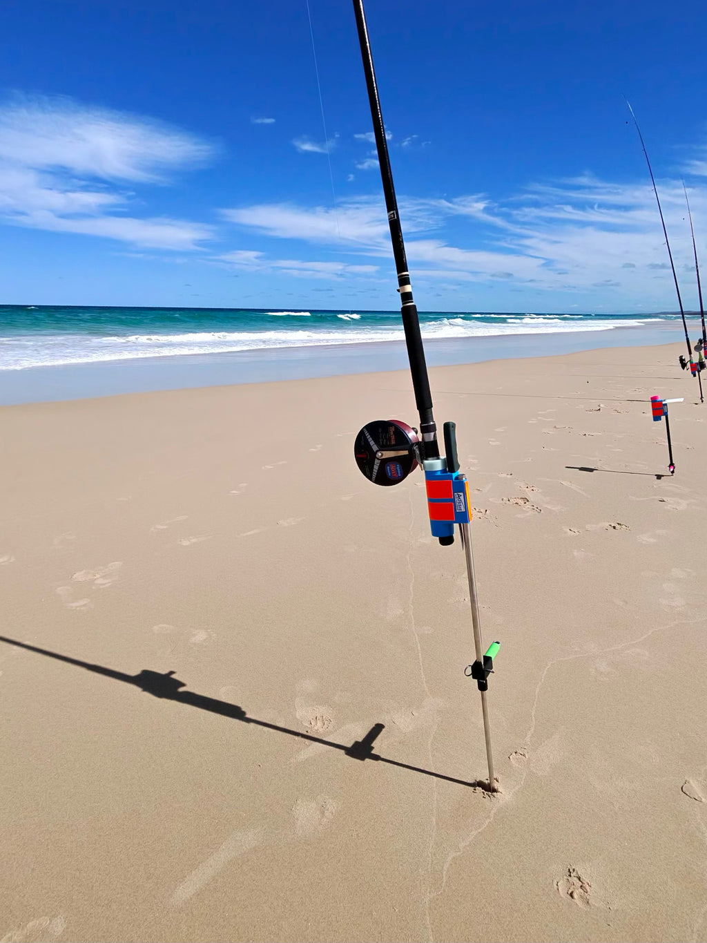 Fishing rod in Aussie Rod Holder on sandy beach with ocean and blue sky in the background