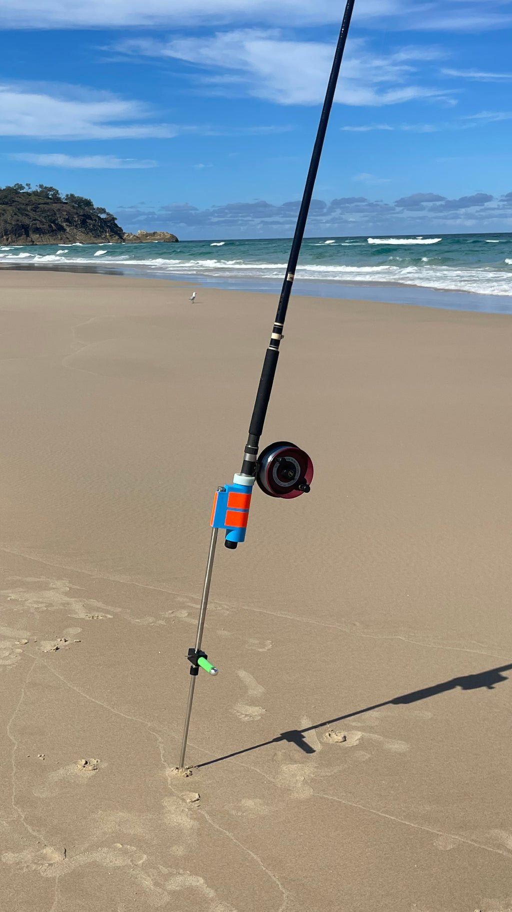 Fishing rod with Alvey reel in rod holder and sand spike at a sandy beach with ocean and sky in the background