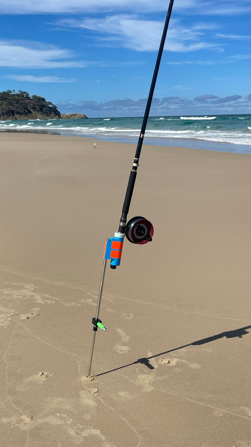 Fishing rod with Alvey reel in rod holder and sand spike at a sandy beach with ocean and sky in the background