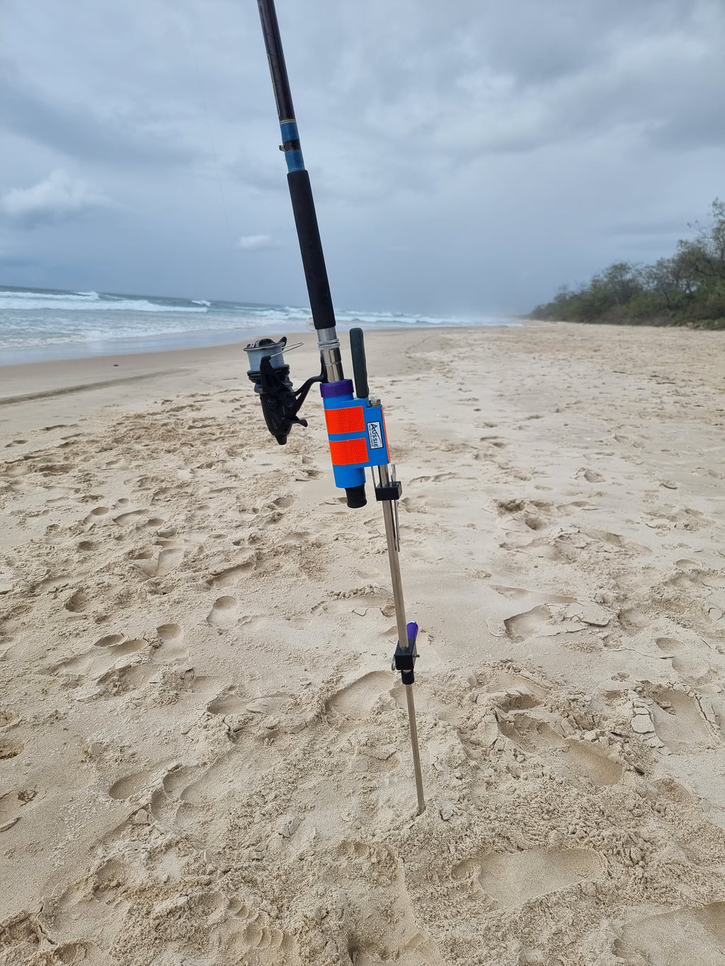 Fishing rod and baitrunner in stainless steel rod holder on beach with fishing knife.