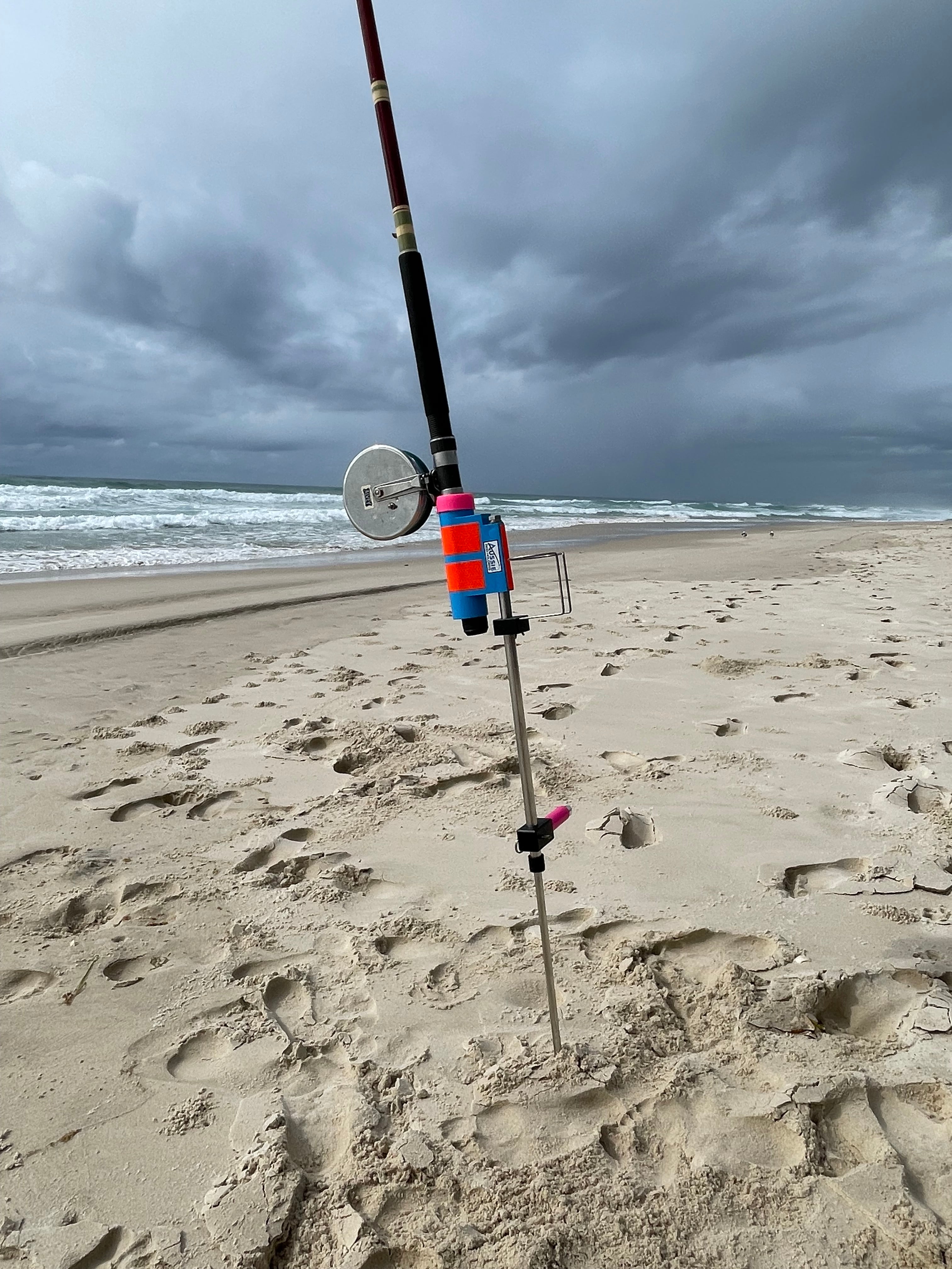 Fishing rod in stainless steel fishing rod holder on a sandy beach with ocean in the background
