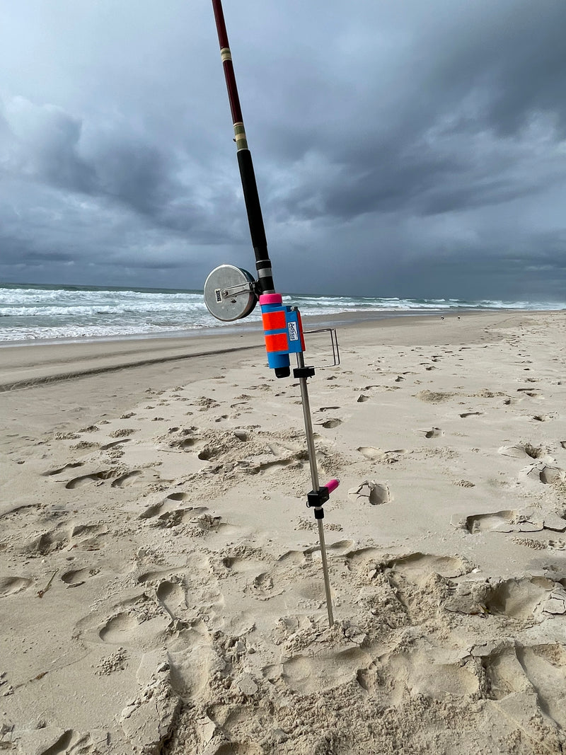 Fishing rod in stainless steel fishing rod holder on a sandy beach with ocean in the background