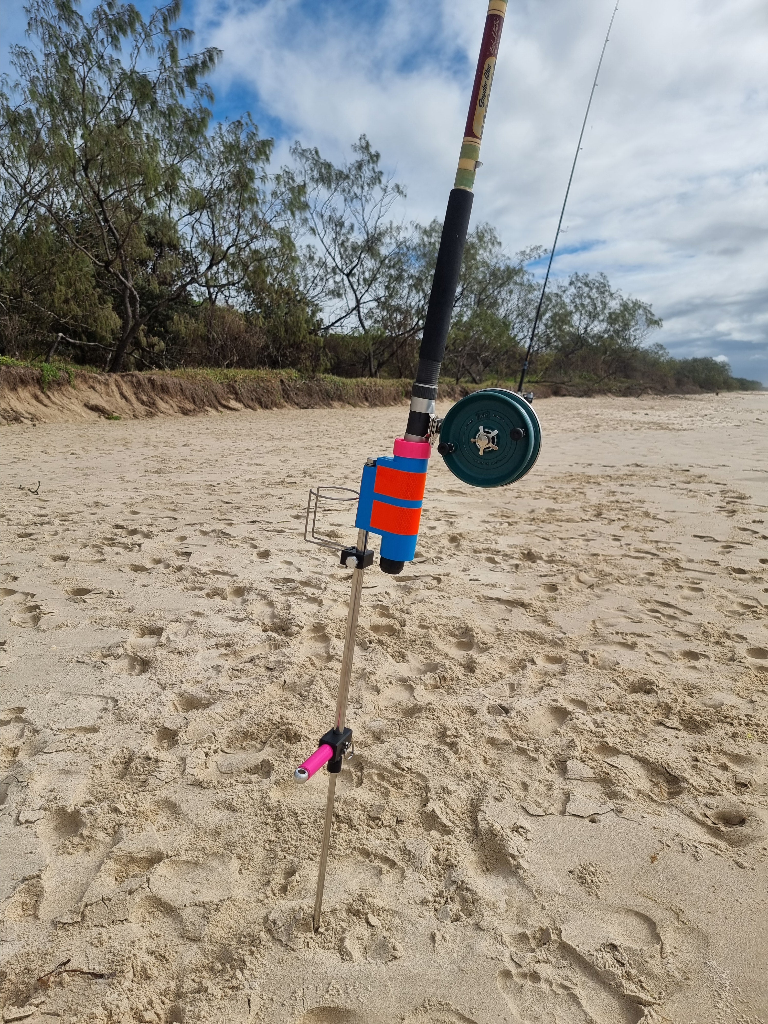 Fishing rod with reel in fishing rod holder with cup holder on a sandy beach