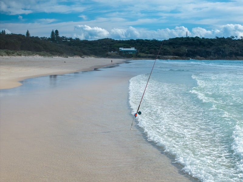 fishing rod and reel in rod holder in the waves of the beach with the headland and surf club in the background