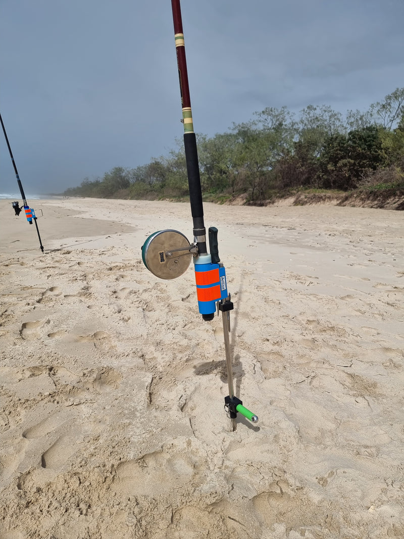 Fishing rod and reel in rod holder on a sandy beach with trees in the background