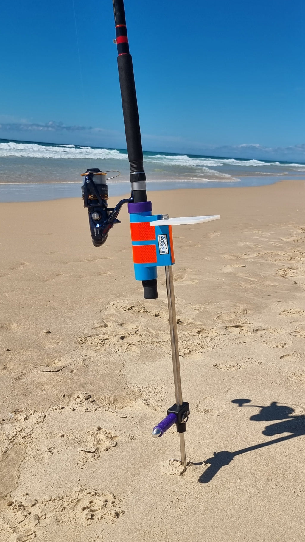Fishing rod with reel in Aussie Rod Holder with bait board on a sandy beach with ocean waves in the background