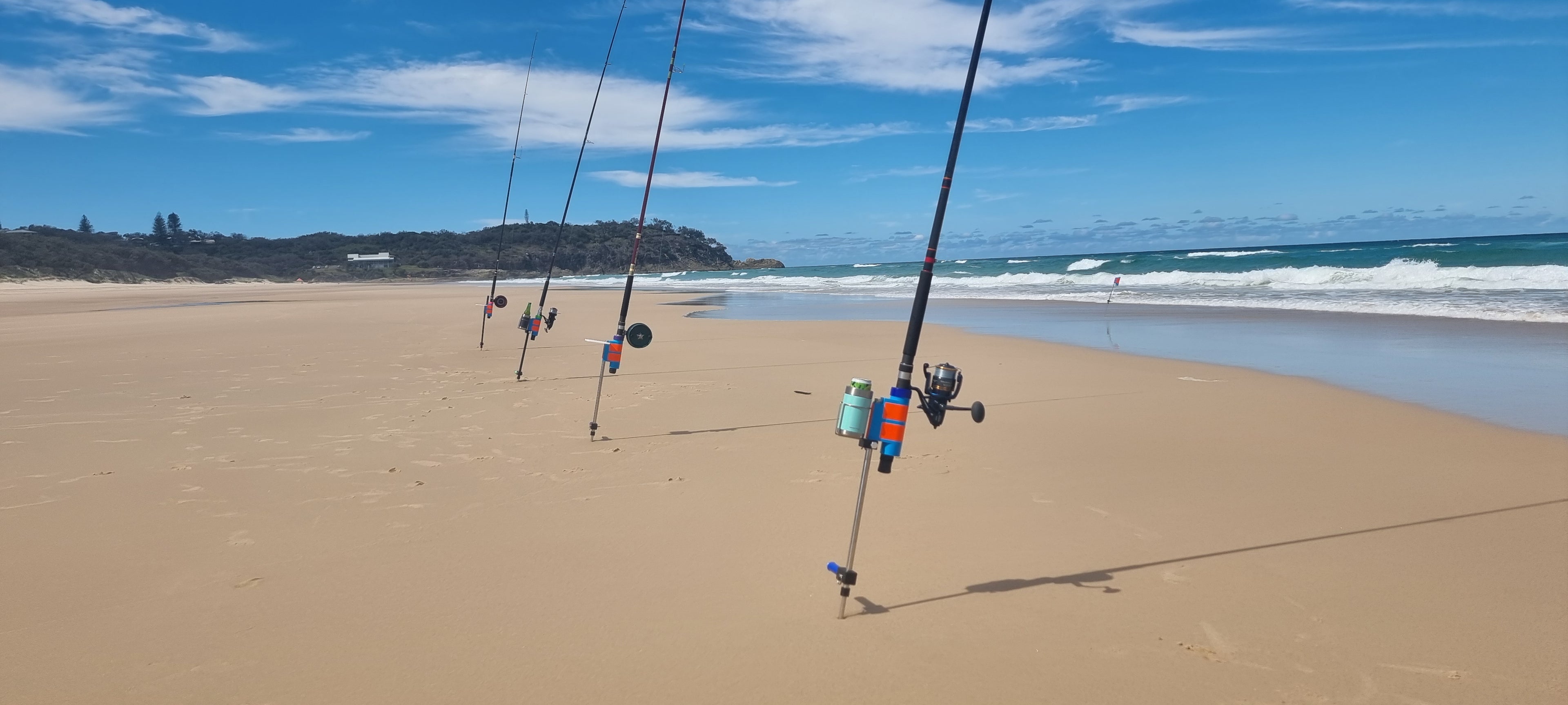 Fishing rods set in fishing rod holders on a sandy Australian beach with ocean and sky in the background